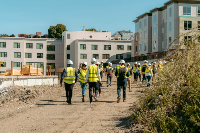 People with yellow vests and hard hats walking through a residential construction zone.