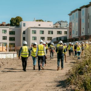 People with yellow vests and hard hats walking through a residential construction zone.